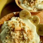 Creamy banana pudding inside a waffle cone bowl with nilla wafers crumbled on top and sliced bananas on the side.