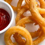 Crispy golden Beer battered onion rings on a white plate with ketchup on the side.