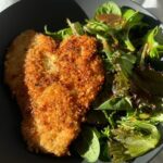 Chicken cutlet with crispy golden breading on a plate next to a green salad.