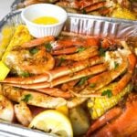 Seafood bake with lobster, crab, shrimp and seasonings in a pan with lemon and butter on the side.