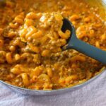 Creamy yellow - orange hamburger helper noodles being scooped with a spoon.