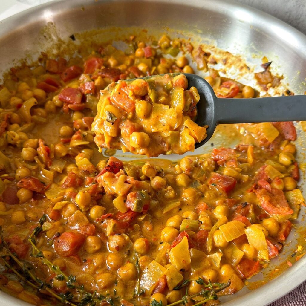 Coconut chickpea curry in a pan being scooped with a spatula.