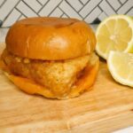 Copycat Filet-o-Fish Sandwich on a wooden cutting board with lemons next to it.