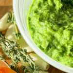 Jamaican green seasoning in a container with garlic, thyme and scotch bonnet pepper on the side.