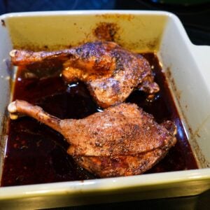 Slow roasted duck legs in a baking dish with red wine sauce.