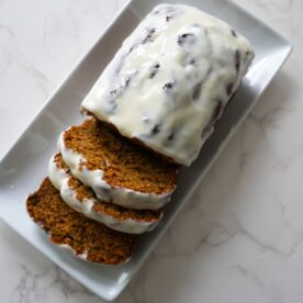 Pumpkin banana bread sliced with cream cheese glaze on a white plate.