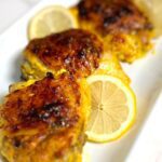 Yogurt marinated chicken thighs on a white plate with sliced lemons.