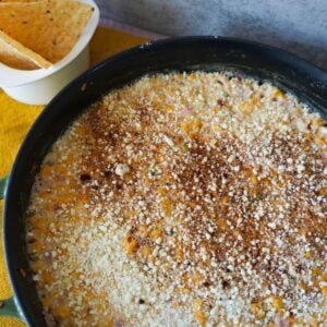 Elote dip inside a cast iron skillet with chips on the side.