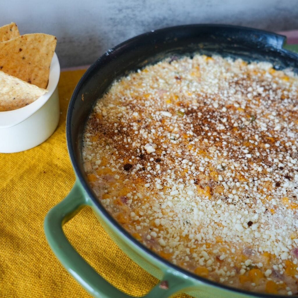Elote dip inside a cast iron skillet with chips on the side.