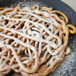 State fair funnel cake on black plate with white powdered sugar.