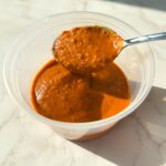 Blended orange chipotle marinade in a container with spoon.