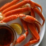 Steamed snow crab legs bright orange on a white plate with a side of cajun butter.