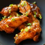 Honey Garlic Chicken Wings on a black plate with scallions on top.