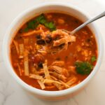 A warm bowl of creamy chicken soup topped with tortilla strips and fresh cilantro.