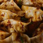 Close up of pork and chive dumplings with mala sauce.