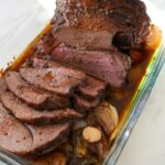 Sliced roasted boneless leg of lamb in a glass baking dish.
