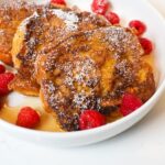 Eggnog French Toast garnished with powdered sugar and maple syrup.