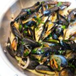 Mussels in white wine sauce in a silver pan.
