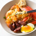 Seafood boil ramen featuring shrimp, crab legs, sausage, ramen noodles, and a Cajun-spiced broth.