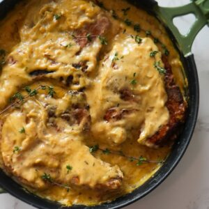Smothered pork chops with creamy gravy and golden onions in a cast iron skillet.