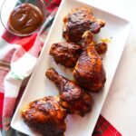 Baked BBQ chicken, glazed with barbecue sauce, served on a white platter.