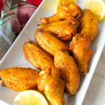 Oven-baked lemon pepper wings coated in a zesty buttery sauce, served with lemon slices.
