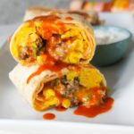 Meal prep breakfast burritos with eggs, sausage, and cheese wrapped in a flour tortilla with hot sauce.