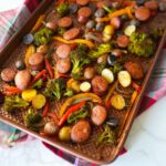 Sheet pan sausage and roasted vegetables with broccoli, bell peppers, potatoes, and onions.