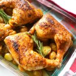 Baked chicken leg quarters with crispy skin and roasted baby potatoes garnished with rosemary.