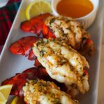 Golden baked lobster tails with garlic butter and fresh parsley on a serving plate.