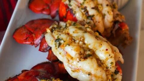 Golden baked lobster tails with garlic butter and fresh parsley on a serving plate.