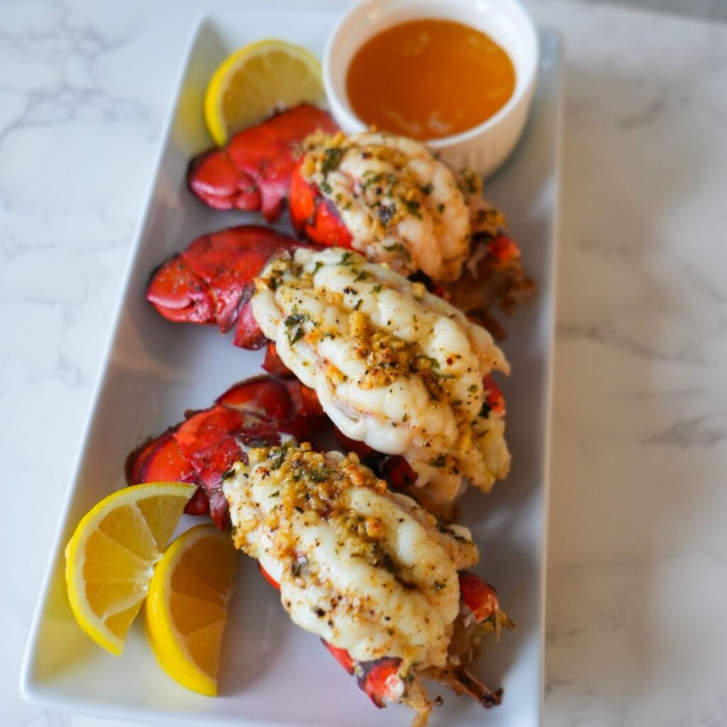 Golden baked lobster tails with garlic butter and fresh parsley on a serving plate.