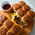 Cheeseburger sliders on Hawaiian rolls topped with melted butter and sesame seeds.