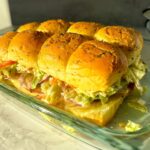 Grinder sliders with melted cheese, deli meats, and crunchy grinder salad on Hawaiian rolls.