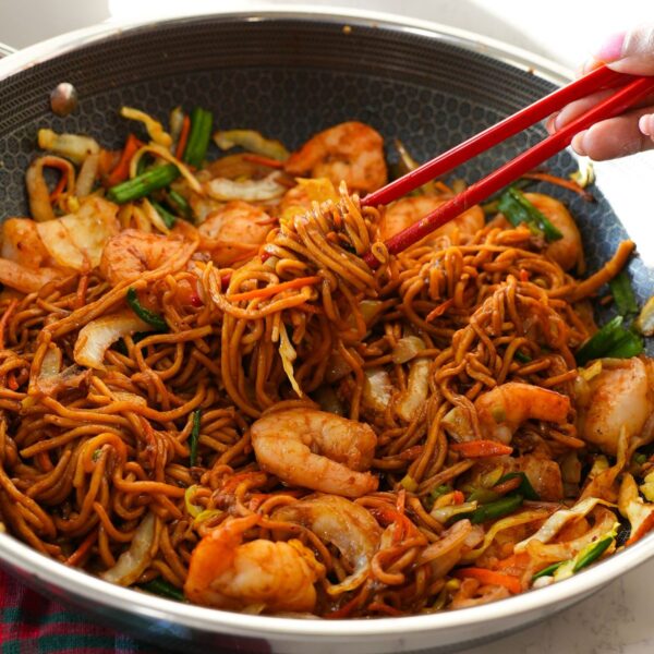 Shrimp lo mein with vegetables and a savory sauce in a pan with chopsticks.