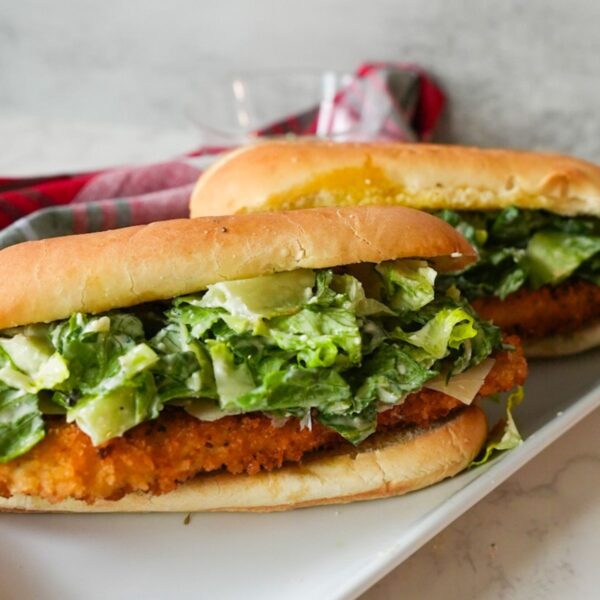 Crispy chicken Caesar salad sandwich on a toasted garlic butter hero roll, served on a plate.