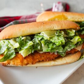 Crispy chicken Caesar salad sandwich on a toasted garlic butter hero roll, served on a plate.