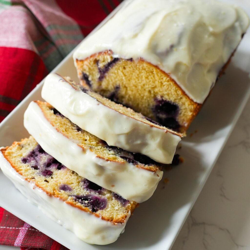 A loaf of lemon blueberry bread with a rich lemon cream cheese glaze, sliced and ready to serve.