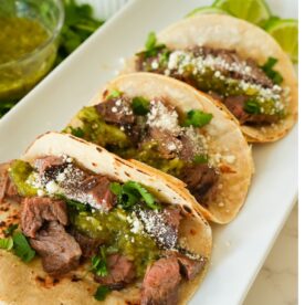 Juicy, grilled skirt steak tacos topped with cotija cheese, salsa verde, and fresh cilantro, served in warm tortillas.