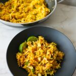 Crab fried rice garnished with fresh herbs, lime wedges, and a drizzle of chili crisp oil.