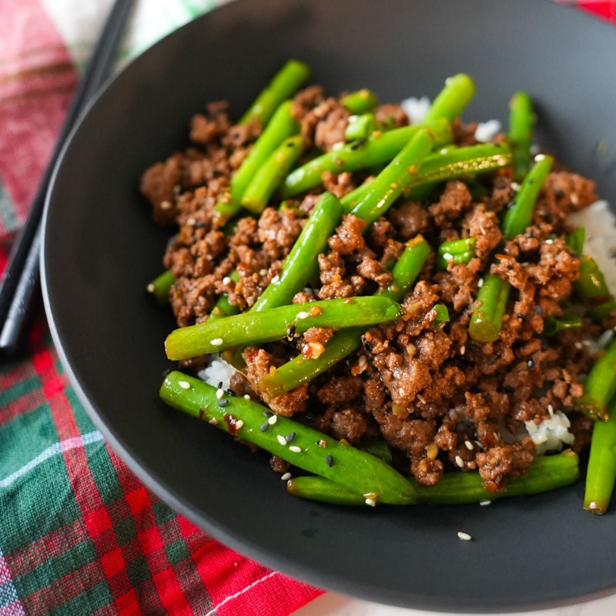 Ground beef stir fry in a bowl on top of rice with chopsticks on the side.
