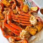 A loaded seafood boil platter topped with Cajun garlic butter, featuring crab legs, shrimp, corn, and lemon wedges.