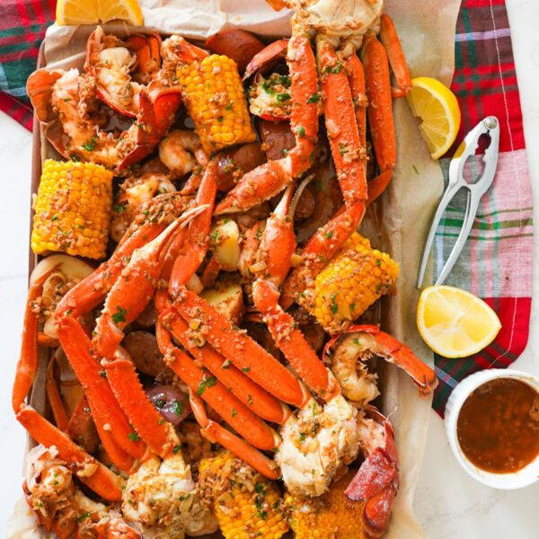 A loaded seafood boil platter topped with Cajun garlic butter, featuring crab legs, shrimp, corn, and lemon wedges.