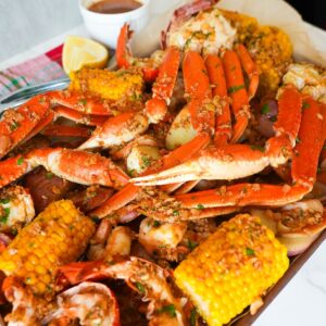 A loaded seafood boil platter topped with Cajun garlic butter, featuring crab legs, shrimp, corn, and lemon wedges.