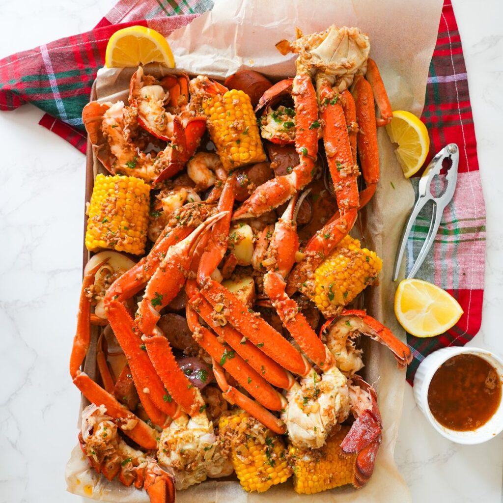 A loaded seafood boil platter topped with Cajun garlic butter, featuring crab legs, shrimp, corn, and lemon wedges.