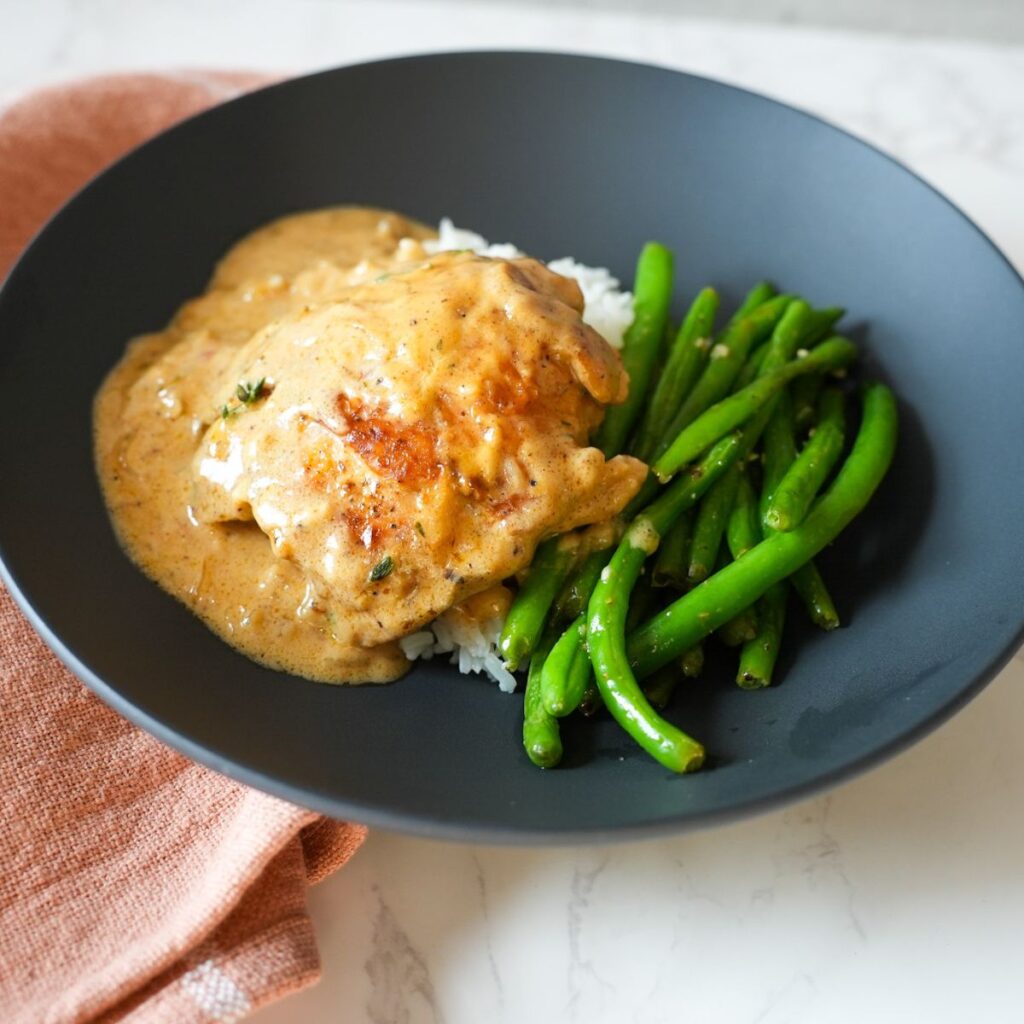 Golden brown chicken thighs simmering in a creamy Cajun onion gravy in a skillet.