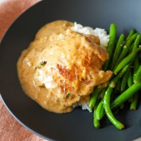 Golden brown chicken thighs simmering in a creamy Cajun onion gravy in a skillet.