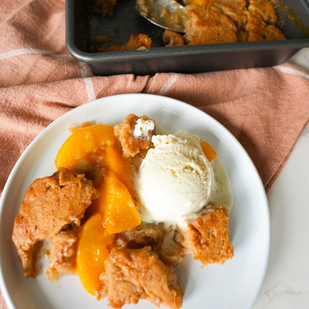 Peach cobbler on a plate with vanilla ice cream.
