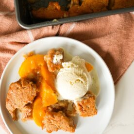 Peach cobbler on a plate with vanilla ice cream.