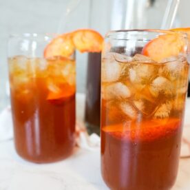 Two glasses of sweet peach tea with ice and fresh peach slices on top.